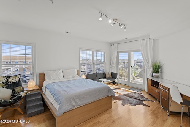 bedroom with access to exterior, track lighting, light hardwood / wood-style floors, and multiple windows