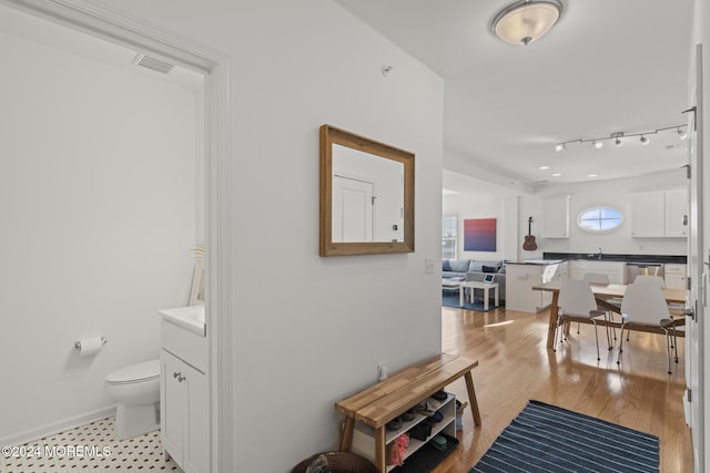 hallway featuring light wood finished floors, baseboards, visible vents, and track lighting