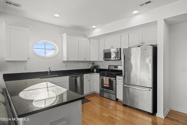 kitchen featuring kitchen peninsula, appliances with stainless steel finishes, sink, white cabinets, and light hardwood / wood-style floors