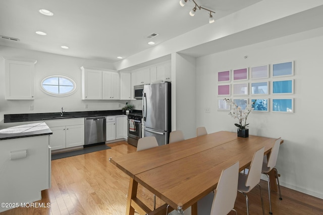 kitchen featuring visible vents, stainless steel appliances, light wood-style floors, white cabinetry, and a sink