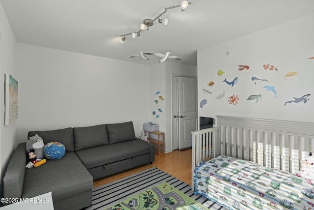 bedroom featuring a nursery area, wood finished floors, and track lighting