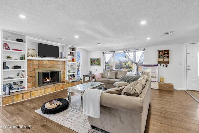 living room with a tiled fireplace, wood-type flooring, and a textured ceiling