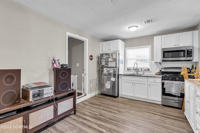 kitchen with white cabinets, sink, light hardwood / wood-style flooring, a textured ceiling, and appliances with stainless steel finishes