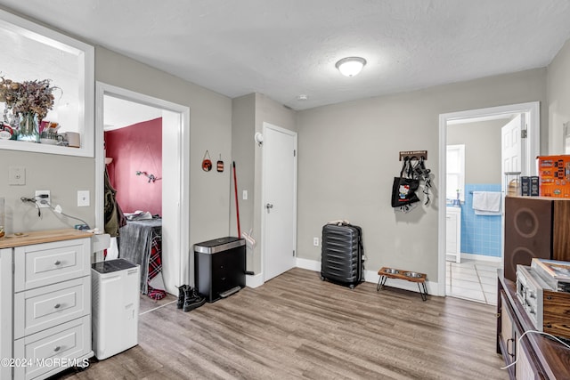 misc room with light wood-type flooring, a textured ceiling, and tile walls