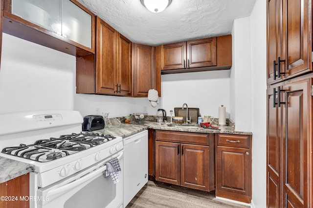 kitchen featuring light stone countertops, a textured ceiling, white appliances, sink, and light hardwood / wood-style flooring