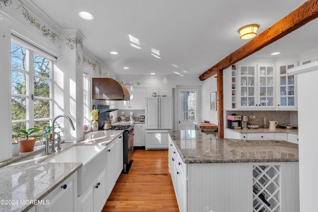 kitchen with a sink, wall chimney range hood, plenty of natural light, and white cabinetry