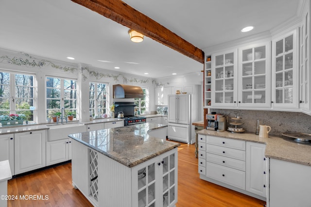 kitchen with paneled refrigerator, beamed ceiling, a sink, wall chimney exhaust hood, and light wood finished floors