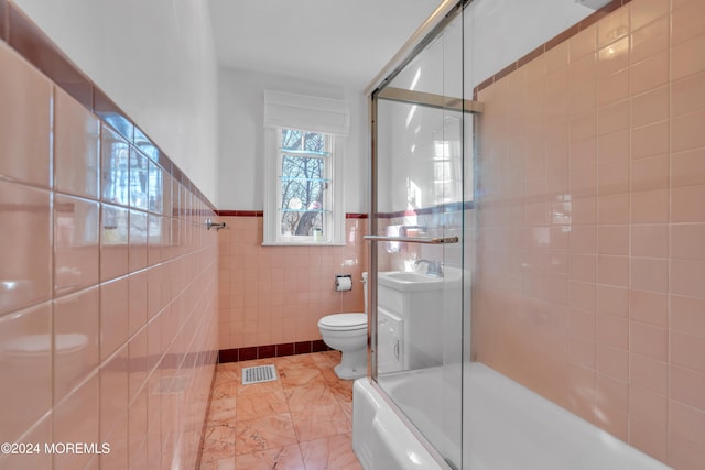 bathroom with visible vents, bath / shower combo with glass door, toilet, tile walls, and a sink