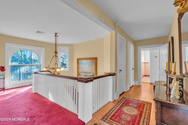 hall with visible vents, baseboards, a chandelier, and light wood finished floors