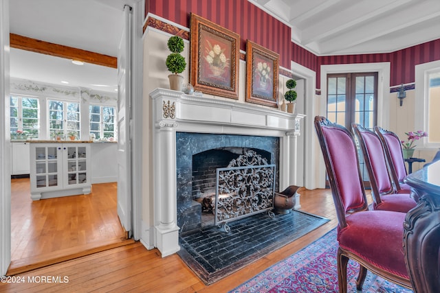 living area with beam ceiling, light wood-style flooring, a high end fireplace, and wallpapered walls