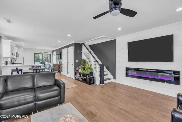 living room with a fireplace, ceiling fan, light hardwood / wood-style flooring, and crown molding