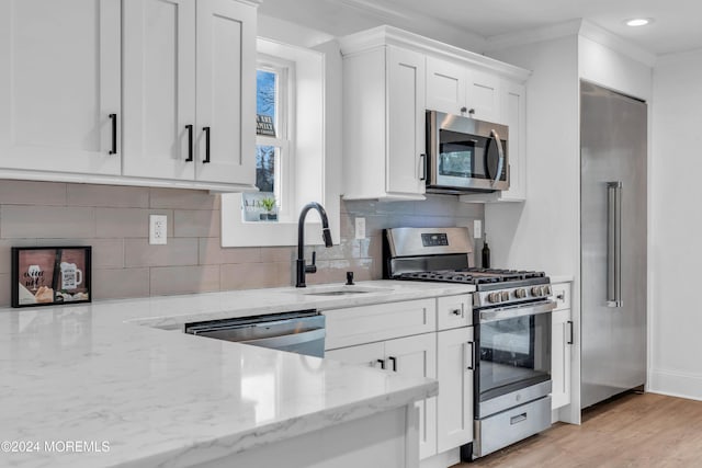 kitchen featuring light wood-type flooring, light stone countertops, ornamental molding, appliances with stainless steel finishes, and white cabinetry