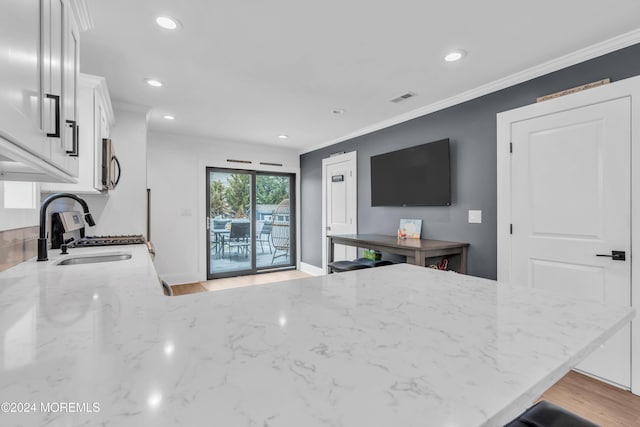 kitchen with kitchen peninsula, light stone countertops, ornamental molding, sink, and white cabinets