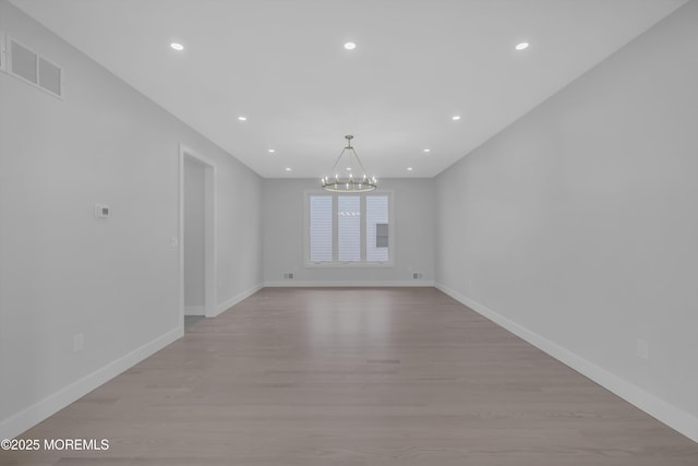 spare room with light hardwood / wood-style flooring and an inviting chandelier