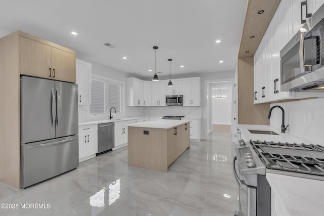 kitchen featuring white cabinetry, sink, a center island, decorative light fixtures, and appliances with stainless steel finishes