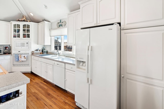 kitchen featuring lofted ceiling, white appliances, a sink, white cabinetry, and light countertops