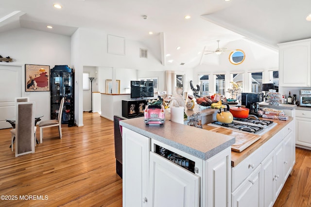 kitchen featuring light wood finished floors, visible vents, a kitchen island, vaulted ceiling, and white gas cooktop