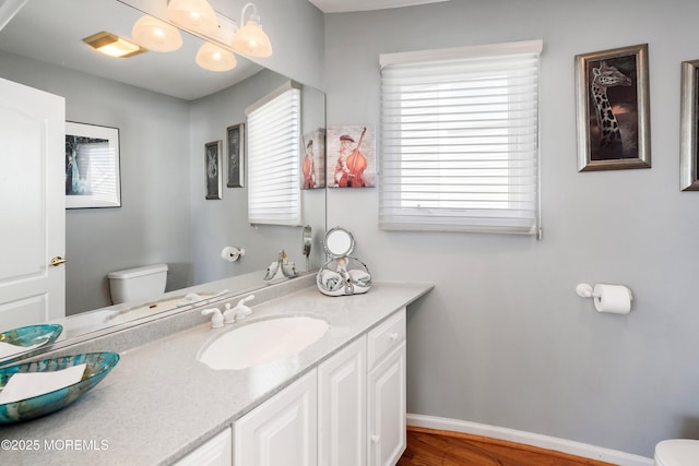 bathroom with baseboards, vanity, toilet, and wood finished floors