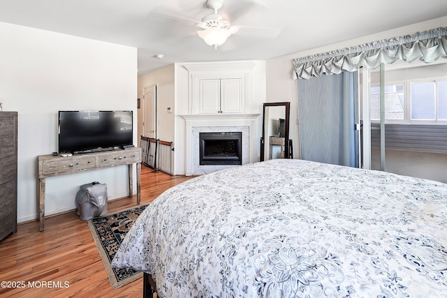 bedroom with a high end fireplace, light wood-type flooring, and ceiling fan