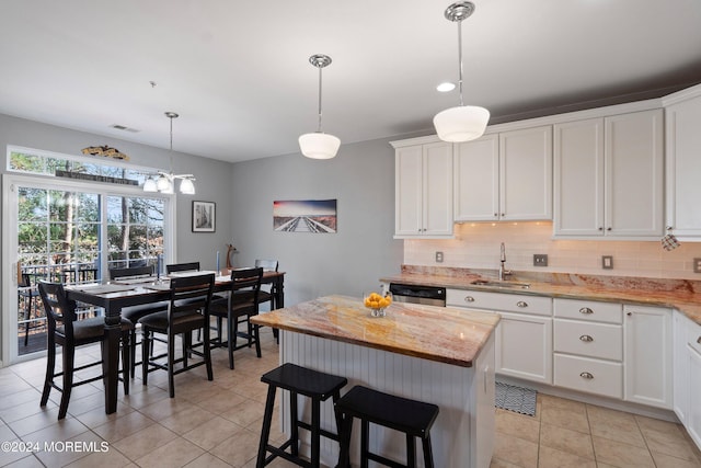 kitchen featuring tasteful backsplash, sink, pendant lighting, white cabinetry, and a kitchen island