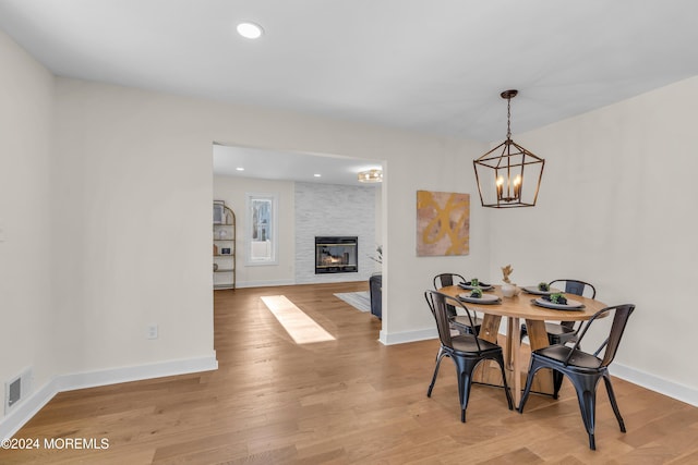 dining space featuring a notable chandelier, a stone fireplace, and light hardwood / wood-style flooring