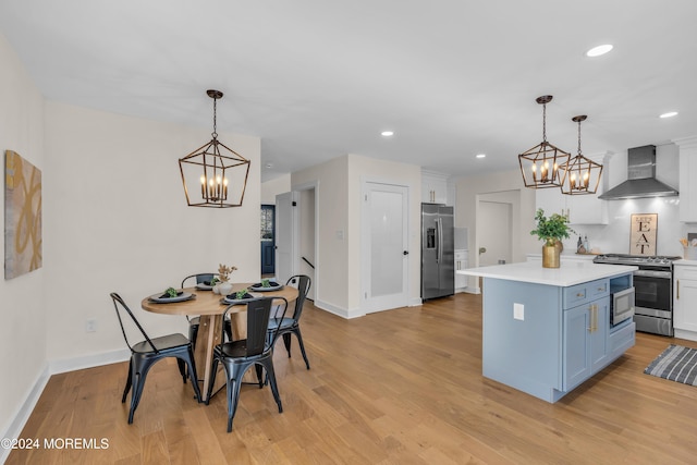 kitchen featuring white cabinets, wall chimney range hood, hanging light fixtures, appliances with stainless steel finishes, and a kitchen island