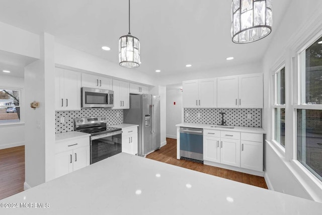 kitchen with hanging light fixtures, white cabinetry, sink, and stainless steel appliances