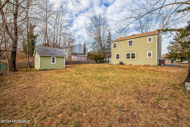 rear view of property with a yard, a storage unit, and central air condition unit