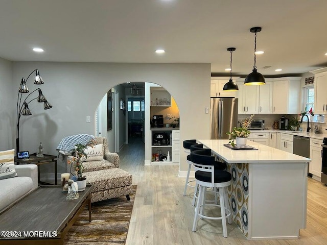 kitchen featuring a center island, light hardwood / wood-style floors, pendant lighting, white cabinets, and appliances with stainless steel finishes