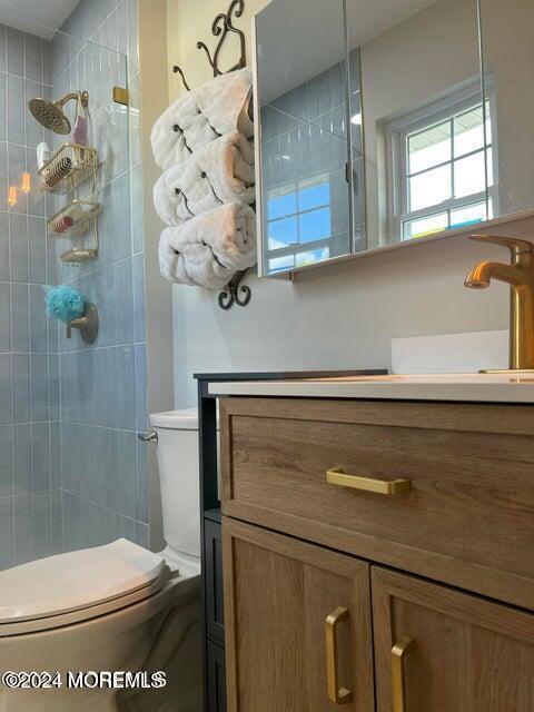 bathroom featuring a tile shower, vanity, and toilet