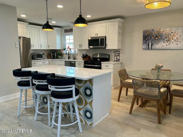 kitchen featuring light wood-type flooring, stainless steel appliances, white cabinetry, and hanging light fixtures