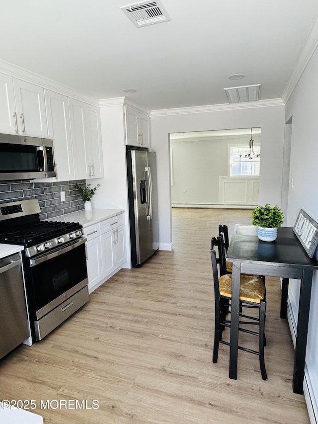 kitchen featuring tasteful backsplash, stainless steel appliances, pendant lighting, a notable chandelier, and white cabinetry