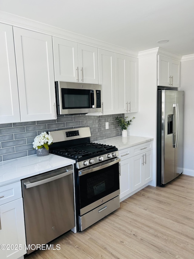 kitchen with light stone countertops, white cabinetry, light hardwood / wood-style floors, and appliances with stainless steel finishes