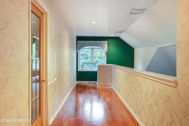 corridor with wood-type flooring and vaulted ceiling