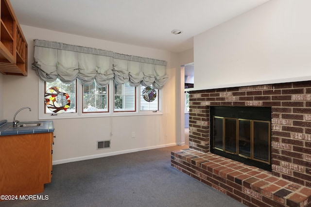 unfurnished living room featuring dark colored carpet, a brick fireplace, and sink