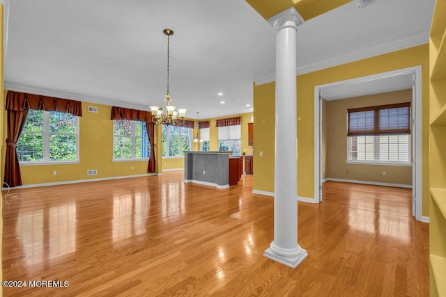 unfurnished living room featuring a notable chandelier, plenty of natural light, and ornate columns