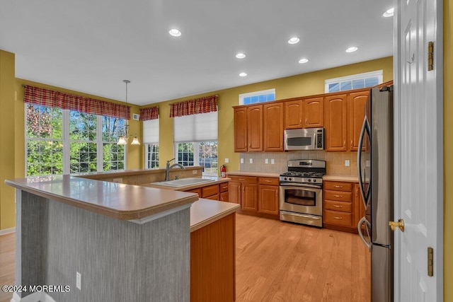 kitchen with hanging light fixtures, sink, decorative backsplash, appliances with stainless steel finishes, and light hardwood / wood-style floors