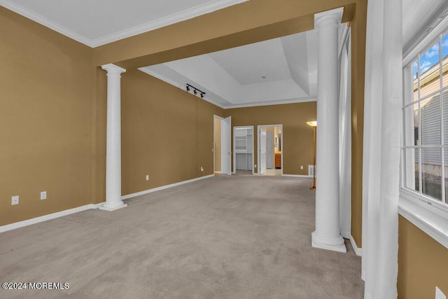 empty room featuring a raised ceiling, light colored carpet, ornate columns, and ornamental molding