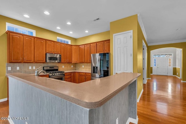 kitchen featuring light hardwood / wood-style flooring, ornamental molding, appliances with stainless steel finishes, tasteful backsplash, and kitchen peninsula