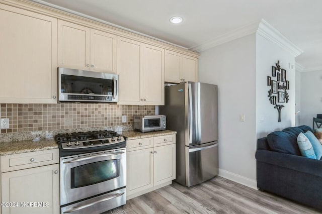 kitchen with light stone countertops, ornamental molding, light wood-type flooring, appliances with stainless steel finishes, and cream cabinetry