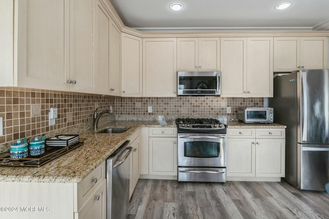 kitchen featuring decorative backsplash, appliances with stainless steel finishes, light hardwood / wood-style floors, and sink