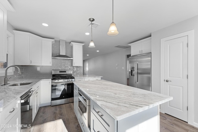 kitchen with white cabinets, wall chimney range hood, sink, appliances with stainless steel finishes, and a kitchen island