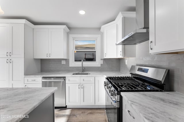 kitchen featuring white cabinetry, wall chimney range hood, sink, and appliances with stainless steel finishes