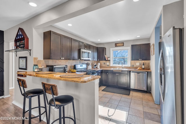 kitchen featuring dark brown cabinetry, backsplash, kitchen peninsula, a kitchen bar, and appliances with stainless steel finishes