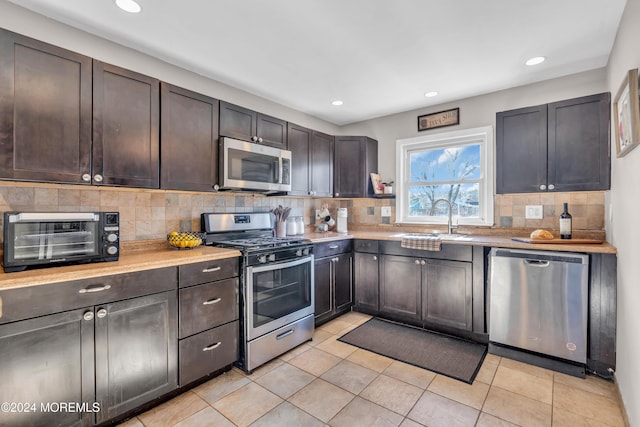 kitchen featuring appliances with stainless steel finishes, backsplash, dark brown cabinetry, sink, and light tile patterned floors