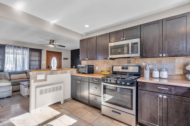 kitchen featuring radiator heating unit, stainless steel appliances, backsplash, kitchen peninsula, and dark brown cabinets