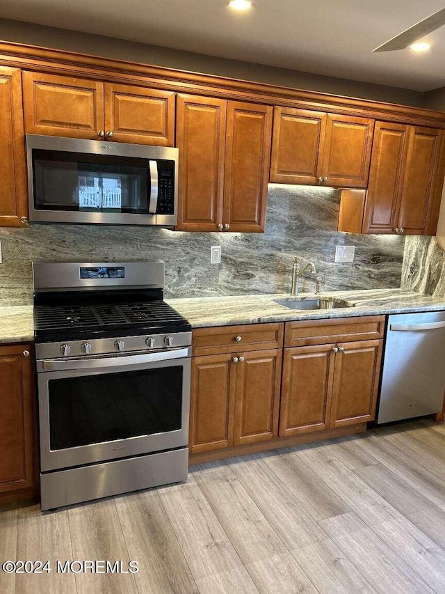 kitchen with backsplash, sink, light wood-type flooring, appliances with stainless steel finishes, and light stone counters