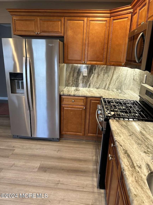 kitchen with backsplash, light hardwood / wood-style floors, light stone countertops, and stainless steel appliances