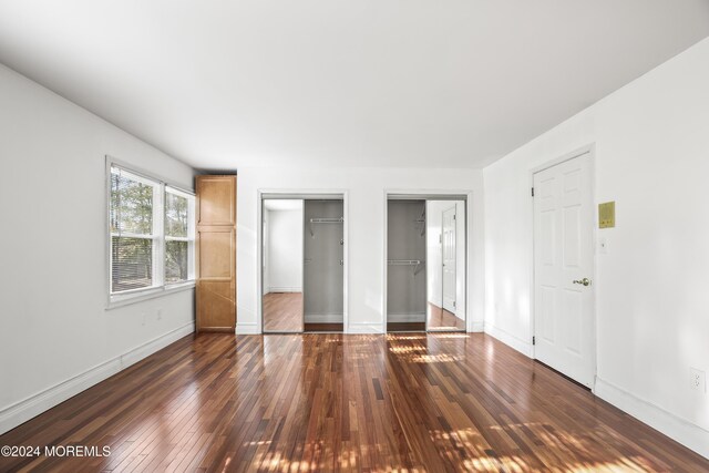 unfurnished bedroom with dark hardwood / wood-style flooring and two closets