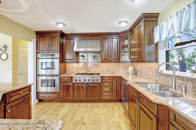 kitchen featuring light stone counters, sink, wall chimney exhaust hood, and stainless steel appliances